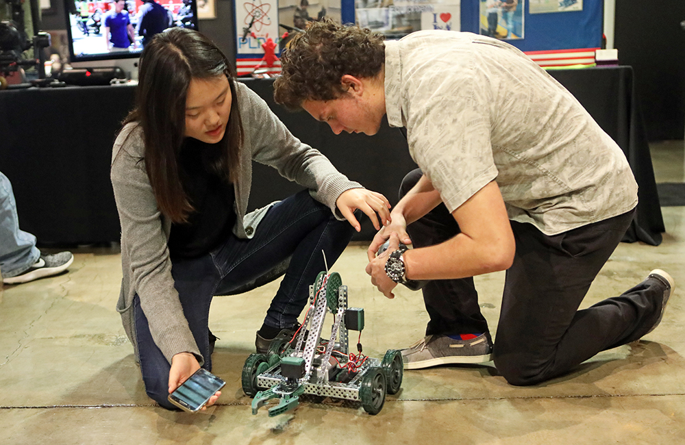a female and male student work on a robotic vehicle while both are hunched over it