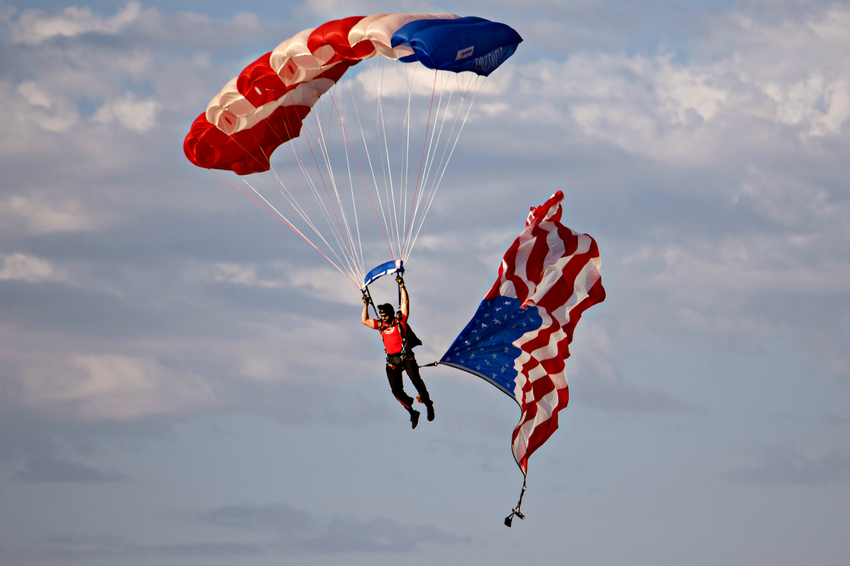 A former Navy SEAL with the Patriot Parachute Team descends onto the field waving a large American flag.