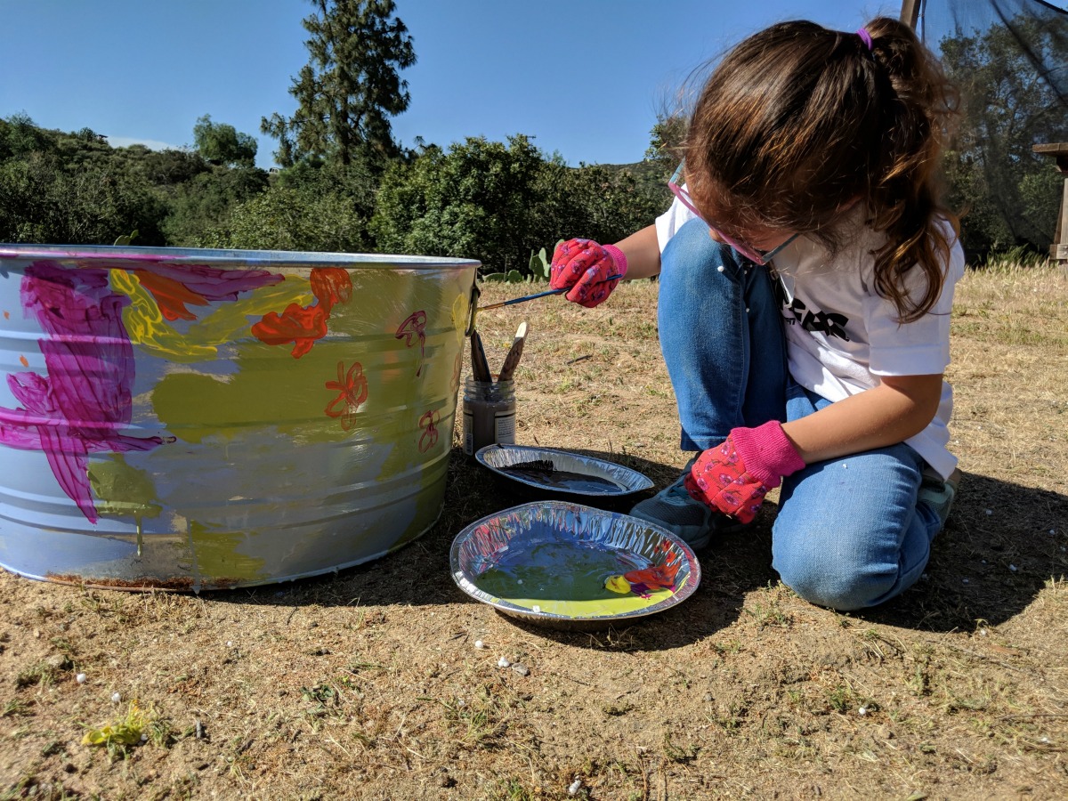 A young girl paints a metal pail.