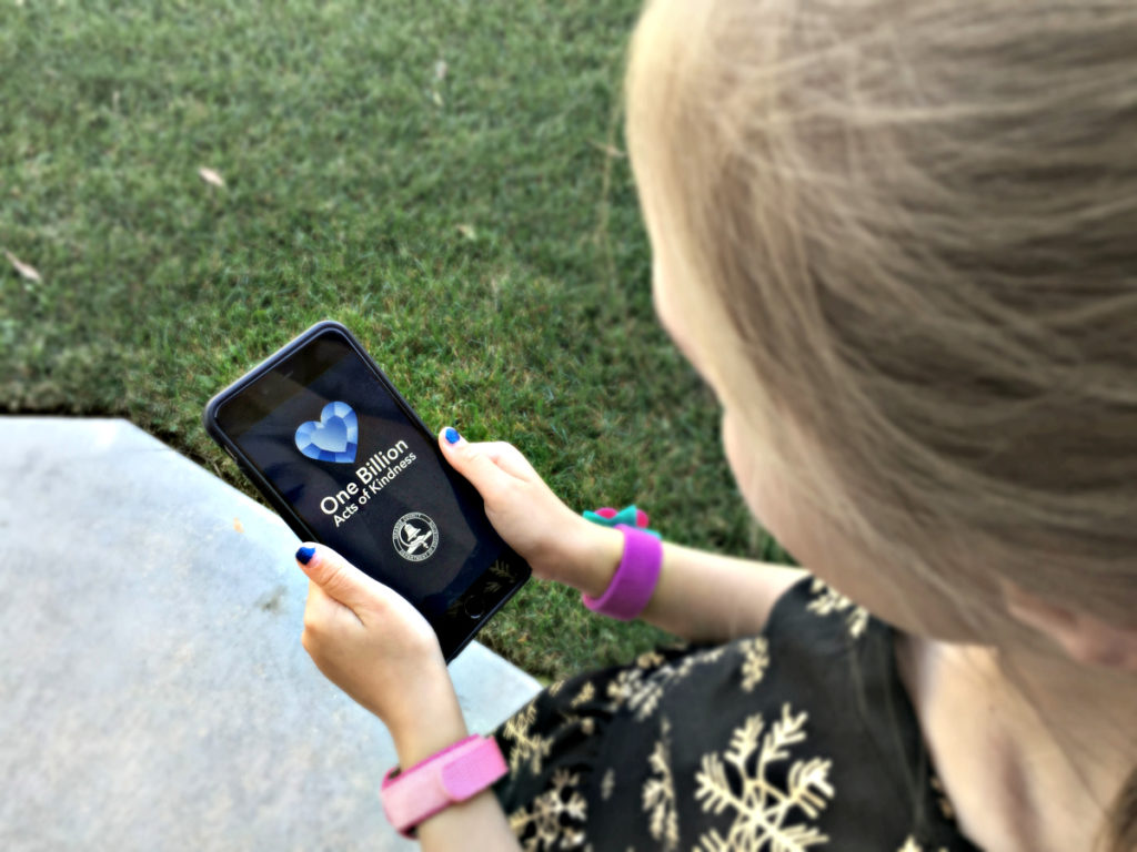 Girl holding iPhone with kindness app