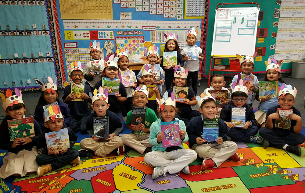 students in a classroom each hold up donated books