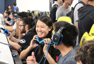 students smiling while sitting at a row of computers playing an online video game