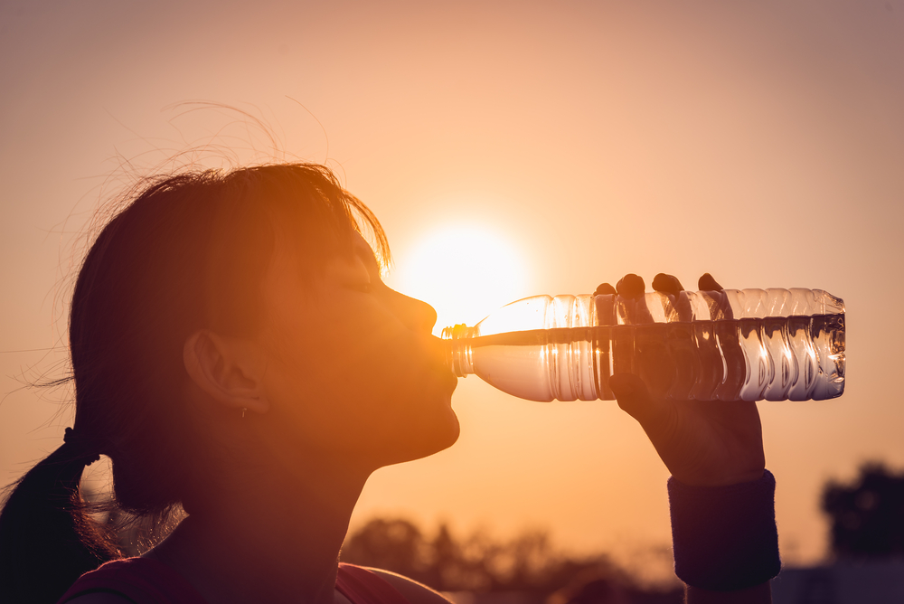 Female drinking a bottle of water with sun in the background