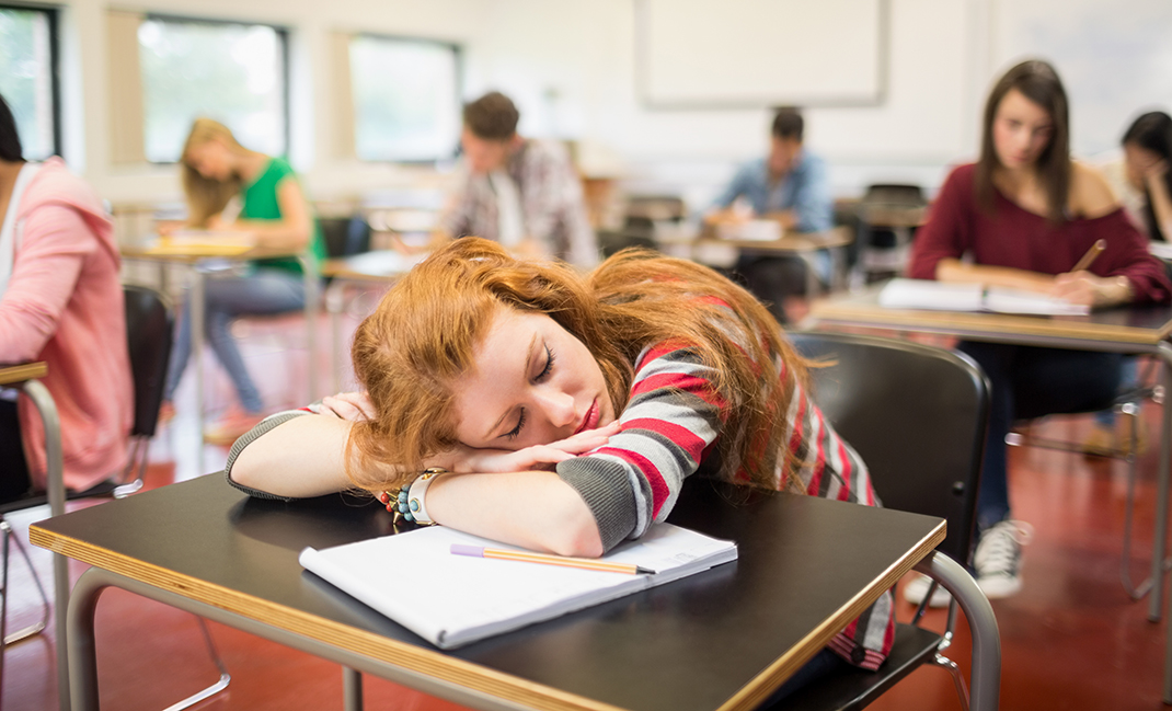 student sleeps on her desk in a classroom
