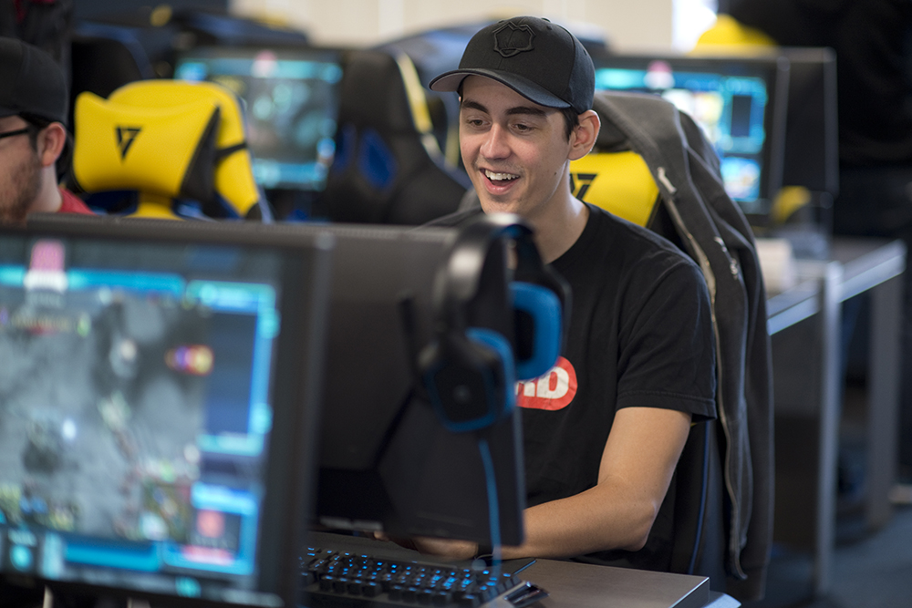 Student with baseball cap smiling and typing on a computer game