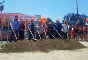 a line of dignitaries hold shovels over a patch of dirt