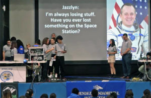 students on stage asking question via audio stream to astronaut