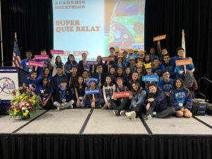 students from five high school academic decathlon teams pose for a photo on a stage