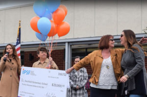 A big check is awarded to a school at an assembly