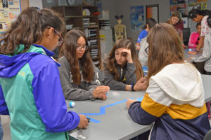 a group of girls sit around a table working on a science project