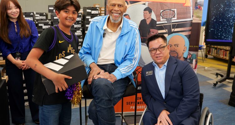 A student in a Lakers jersey stands beside Kareem Abdul-Jabbar and Dr. Stefan Bean
