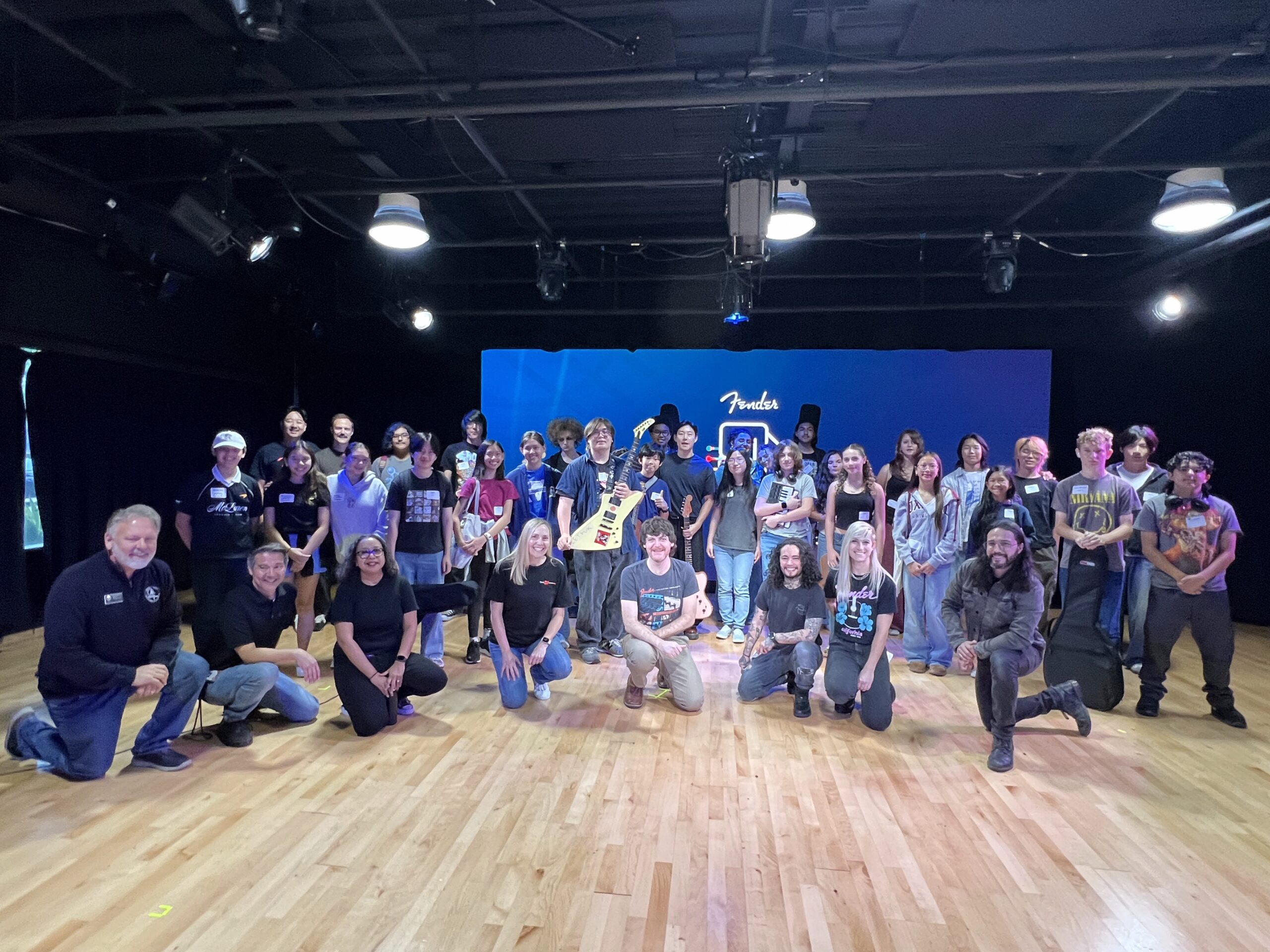 A large group of high school students and adult organizers pose together on stage at OC Music & Dance during the Fender Play songwriting workshop.