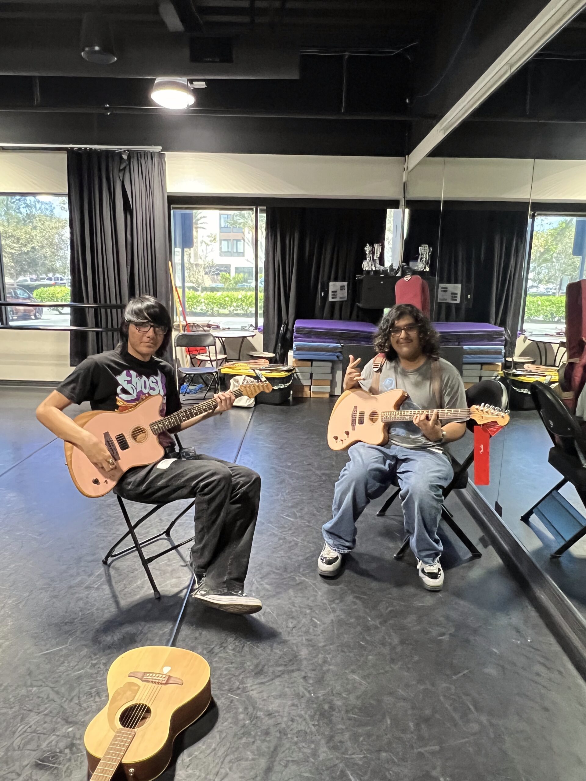 Two high school students sit with guitars in a rehearsal space during the Fender Play songwriting workshop at OC Music & Dance.