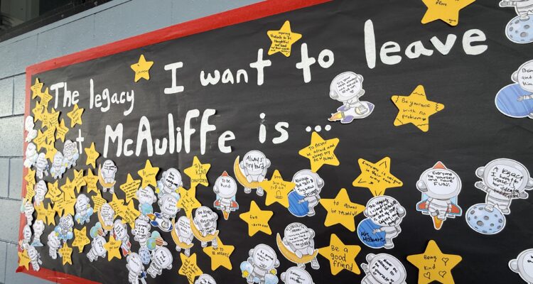 A student-created display at McAuliffe Middle School shows handwritten reflections on paper stars and astronaut cutouts under the message, “The legacy I want to leave at McAuliffe is …”