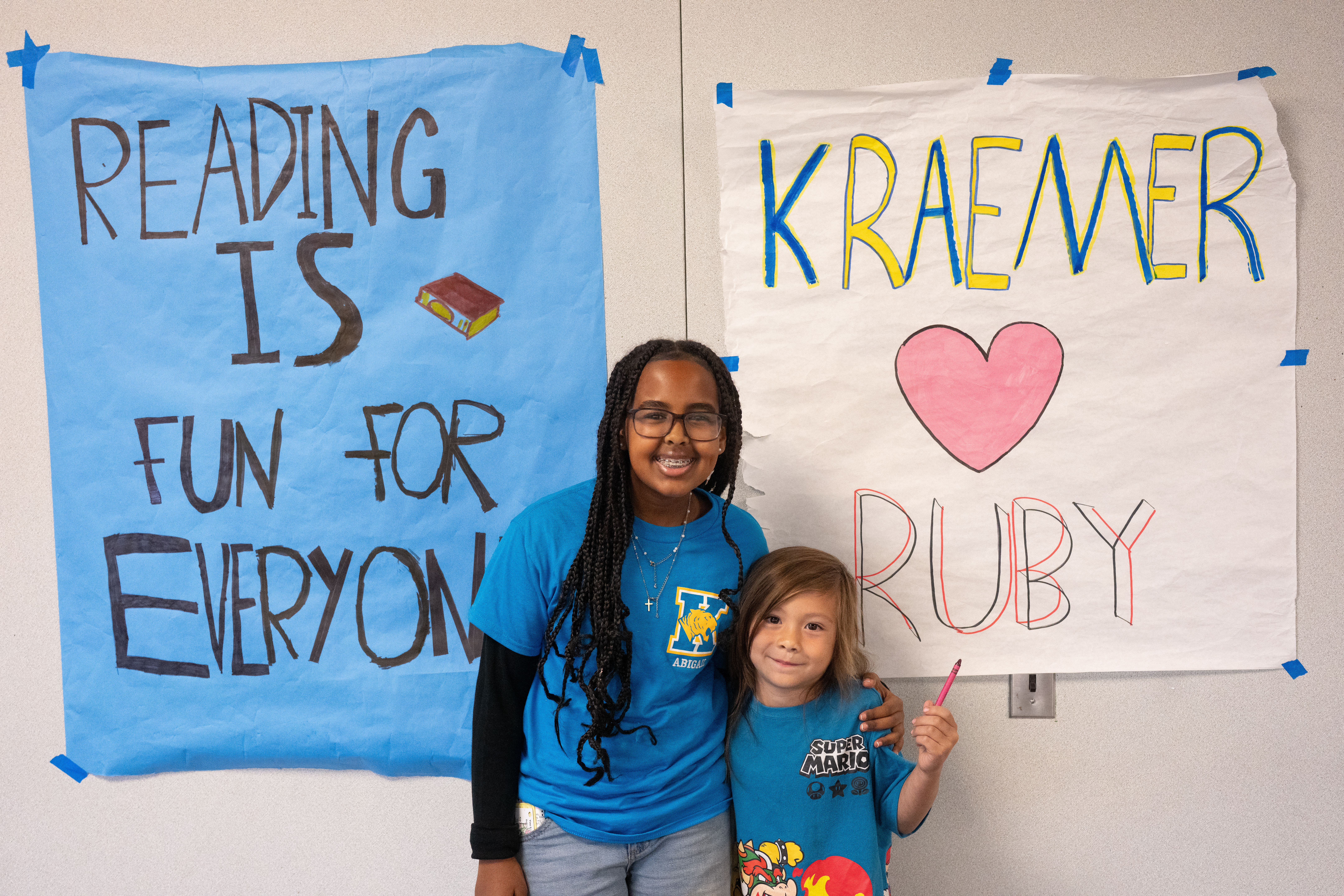 Reading buddies stand in front of a student-made poster that reads, “Kraemer loves Ruby.”