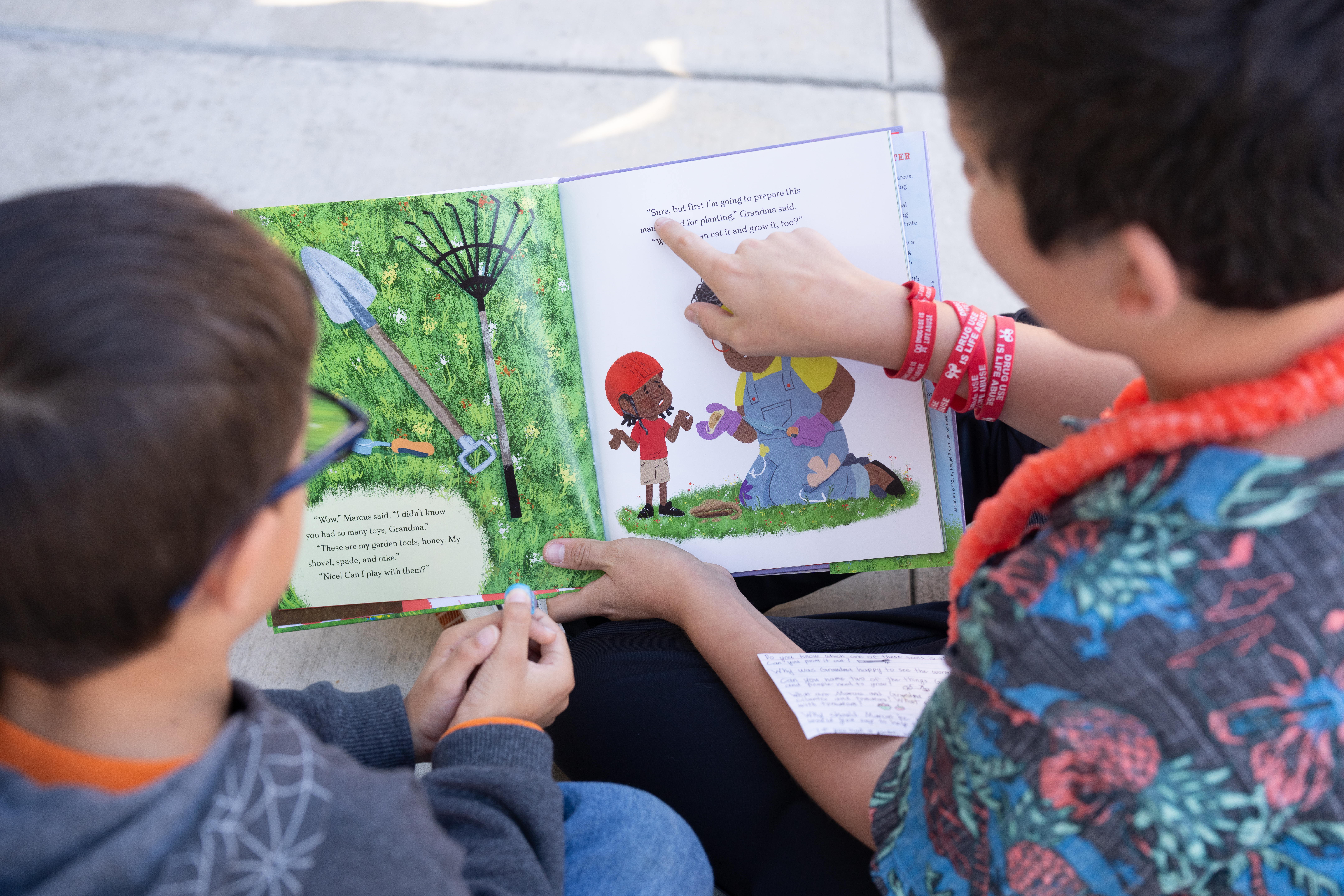 An older student reads to a younger buddy, pointing out words as they go.