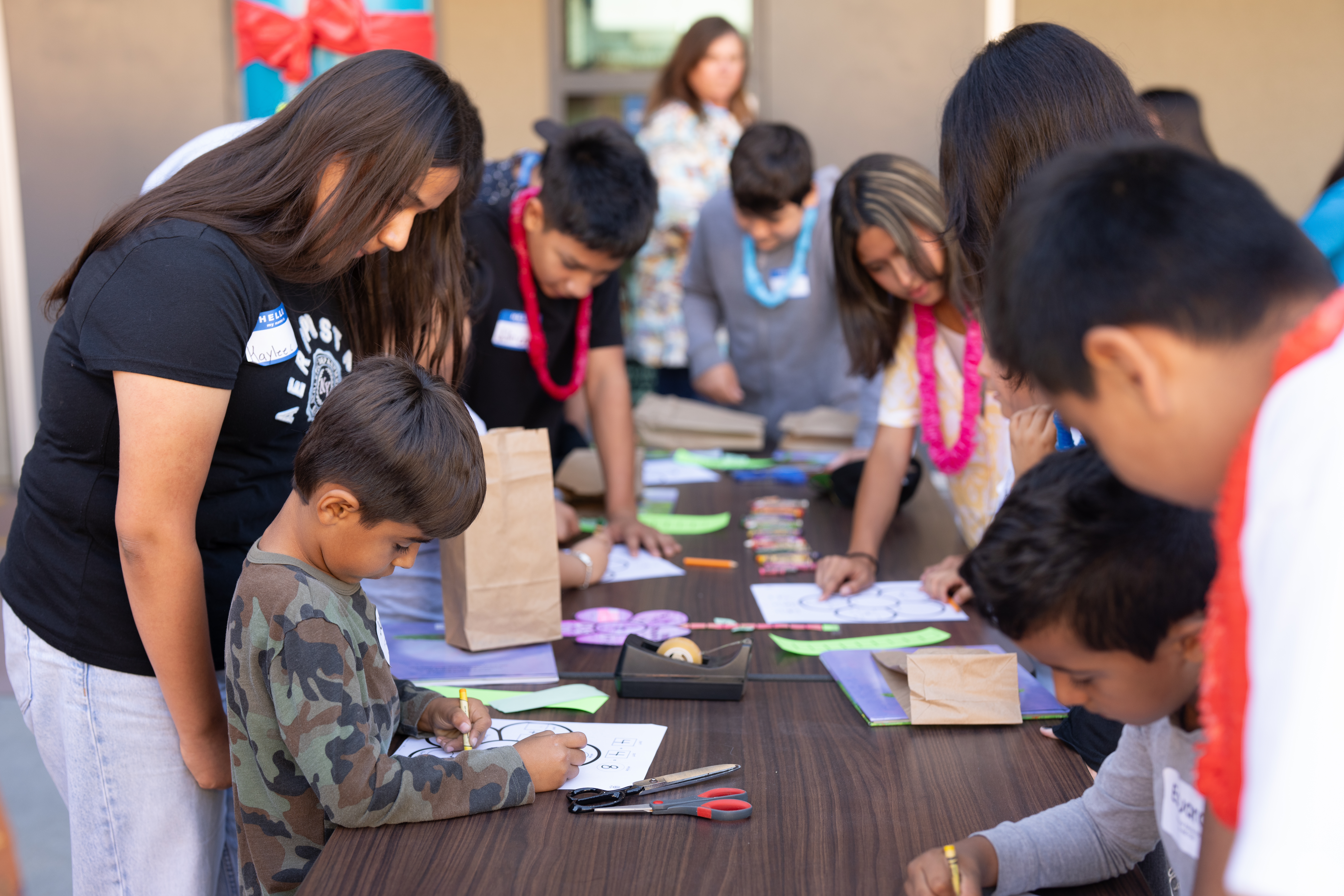 Older buddies stand beside their younger partners at the art activity table.