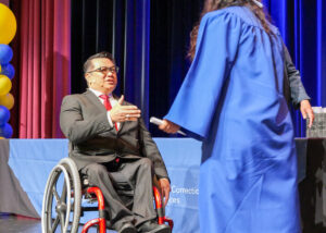 Dr. Stefan Bean reaches out to shake hands with an ACCESS graduate in a blue gown during a commencement ceremony.