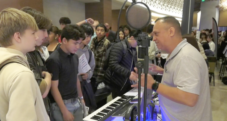 Students interact with an industry professional at a Future Leaders Conference exhibit, featuring a keyboard, microphone, and other tools for hands-on learning and career exploration.