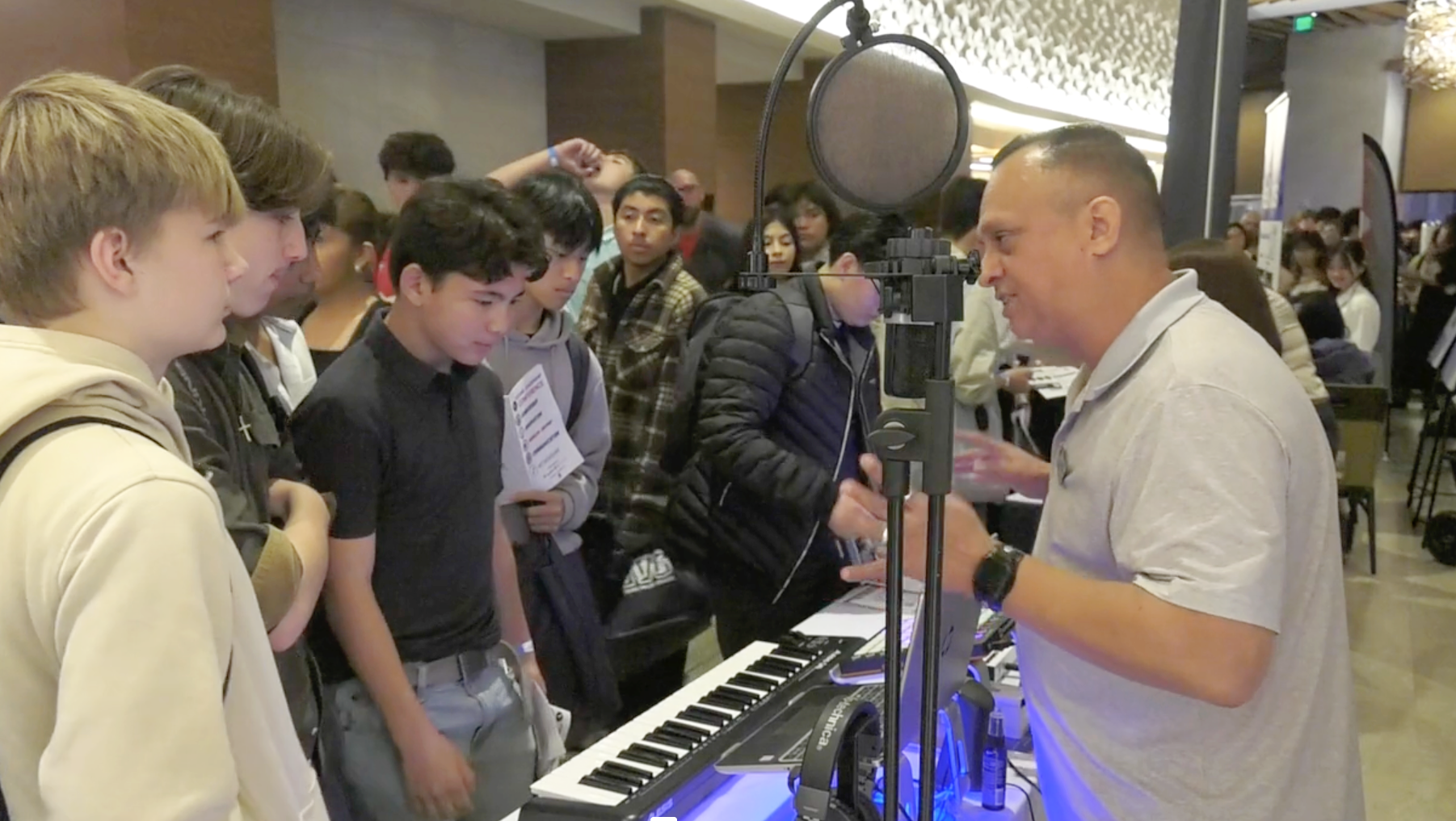 Students interact with an industry professional at a Future Leaders Conference exhibit, featuring a keyboard, microphone, and other tools for hands-on learning and career exploration.