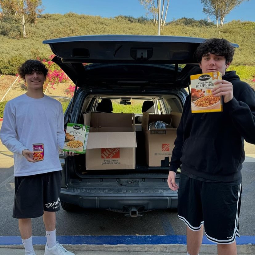 Two students stand by an SUV with food donations for a school food drive