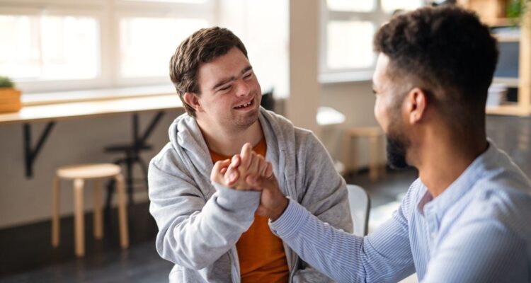 Two individuals smiling and clasping hands in a supportive gesture