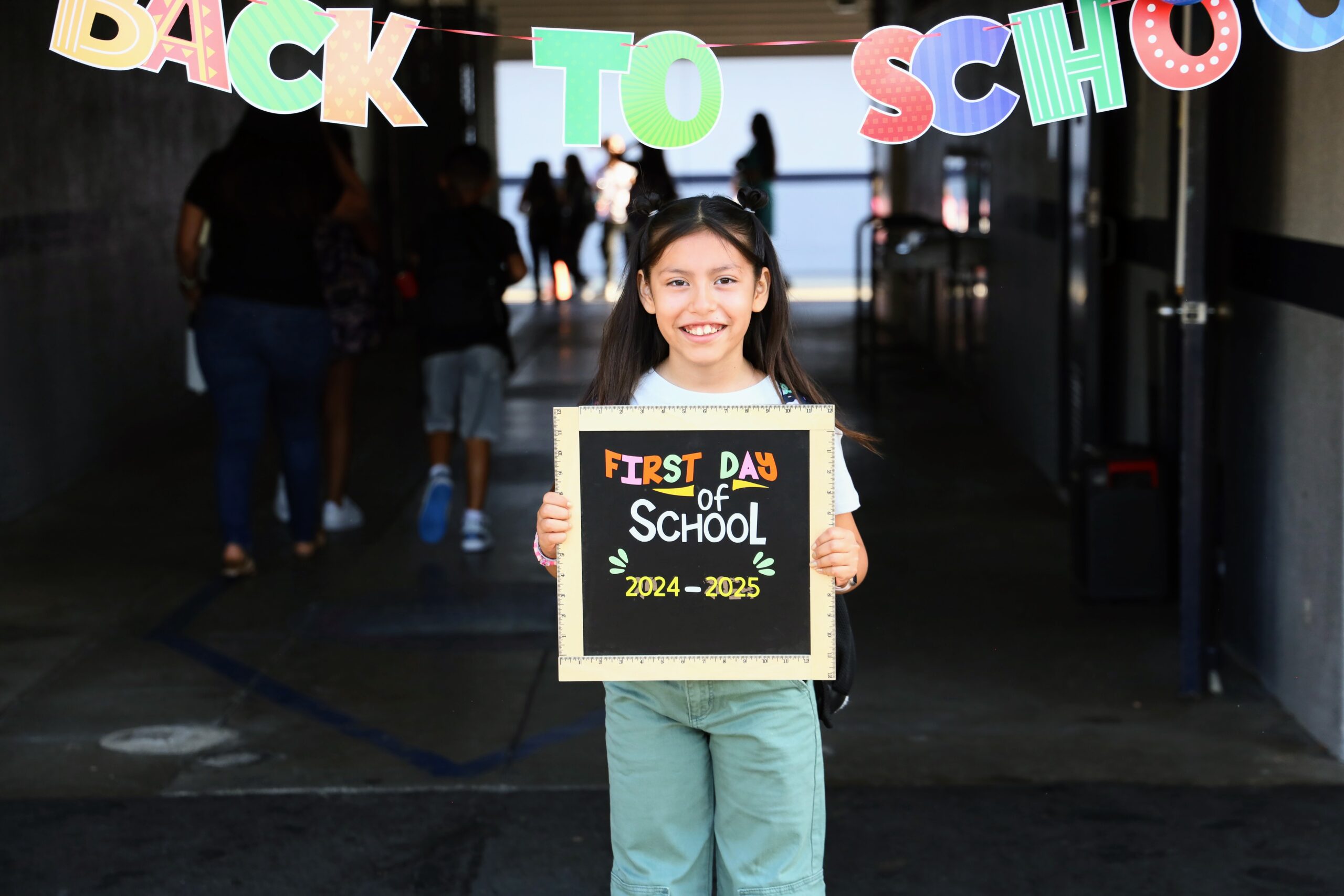 Girl holding "First Day of School" sign from 2024