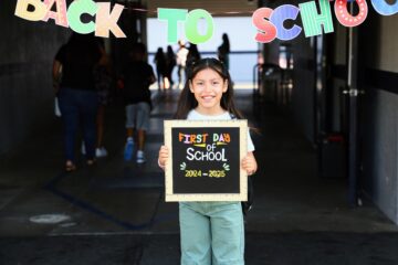 Girl holding "First Day of School" sign from 2024