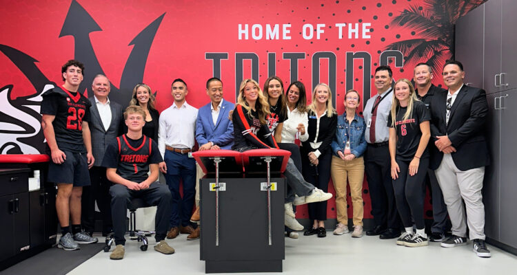 Group of San Clemente High School student-athletes and representatives from Hoag and Capistrano Unified School District standing and smiling inside the school’s new athletic training room, featuring a bright red wall with the words “Home of the Tritons.”