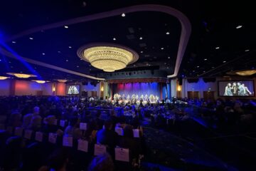 Brea Olinda High School’s Masquerade show choir performs on stage under colorful lighting during the 2026 Orange County Teachers of the Year gala at the Disneyland Hotel, with guests seated at round tables throughout the ballroom.