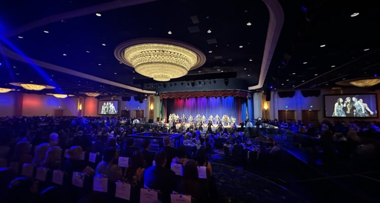 Brea Olinda High School’s Masquerade show choir performs on stage under colorful lighting during the 2026 Orange County Teachers of the Year gala at the Disneyland Hotel, with guests seated at round tables throughout the ballroom.