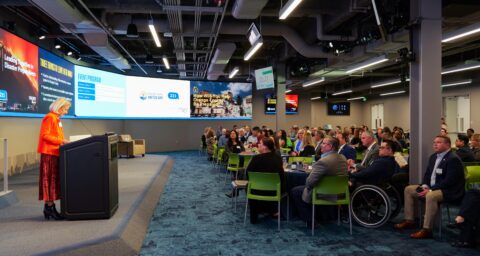 Sue Parks stands at a podium addressing an audience during the Be Prepared OC Summit at the UC Irvine Beall Applied Innovation Center.