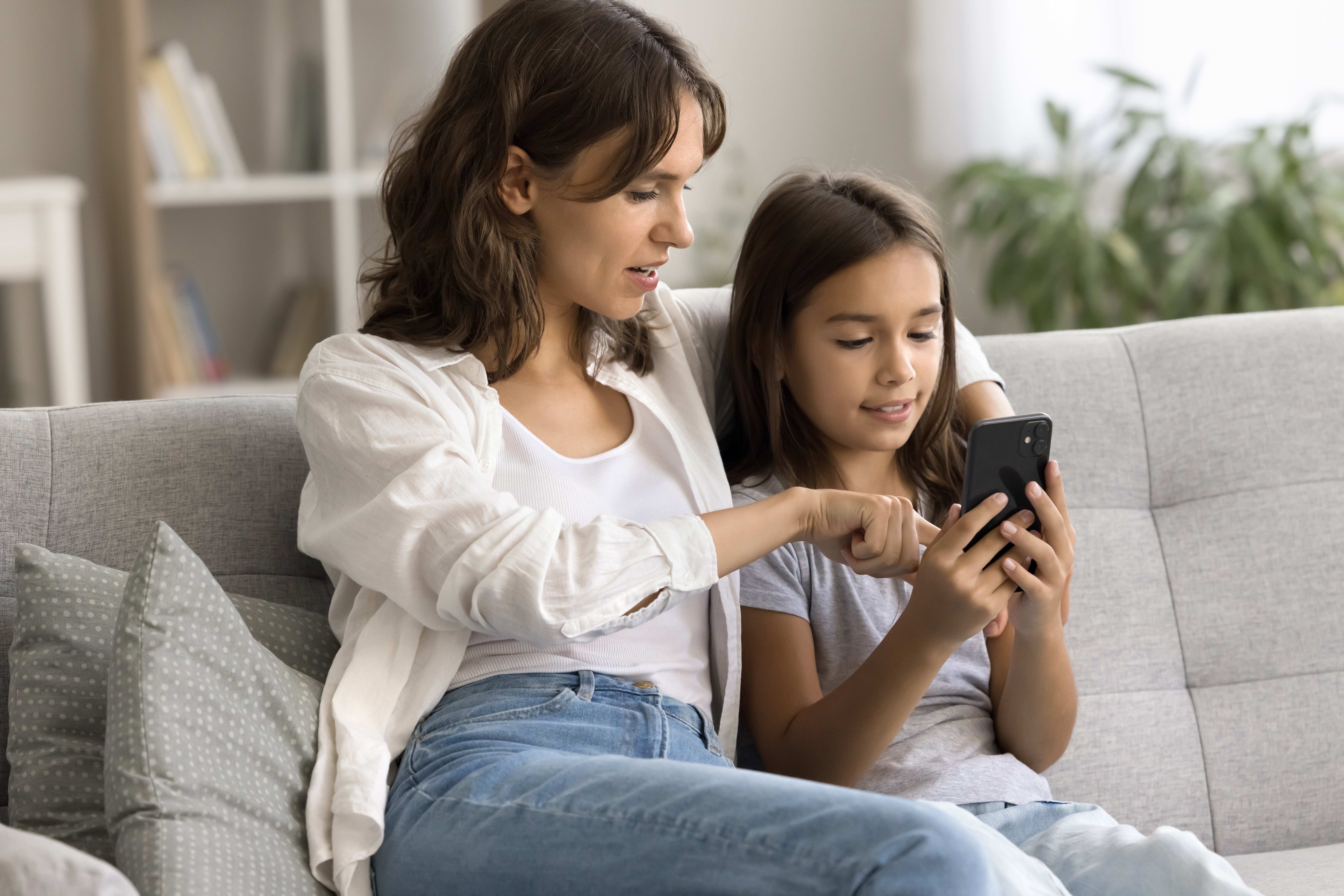 Mother and daughter sitting on a couch looking at a smartphone together