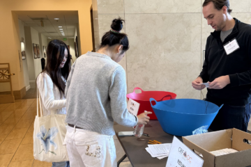 High school students return surveys at a registration table during the Law Day Conference at Chapman University while a volunteer assists them.