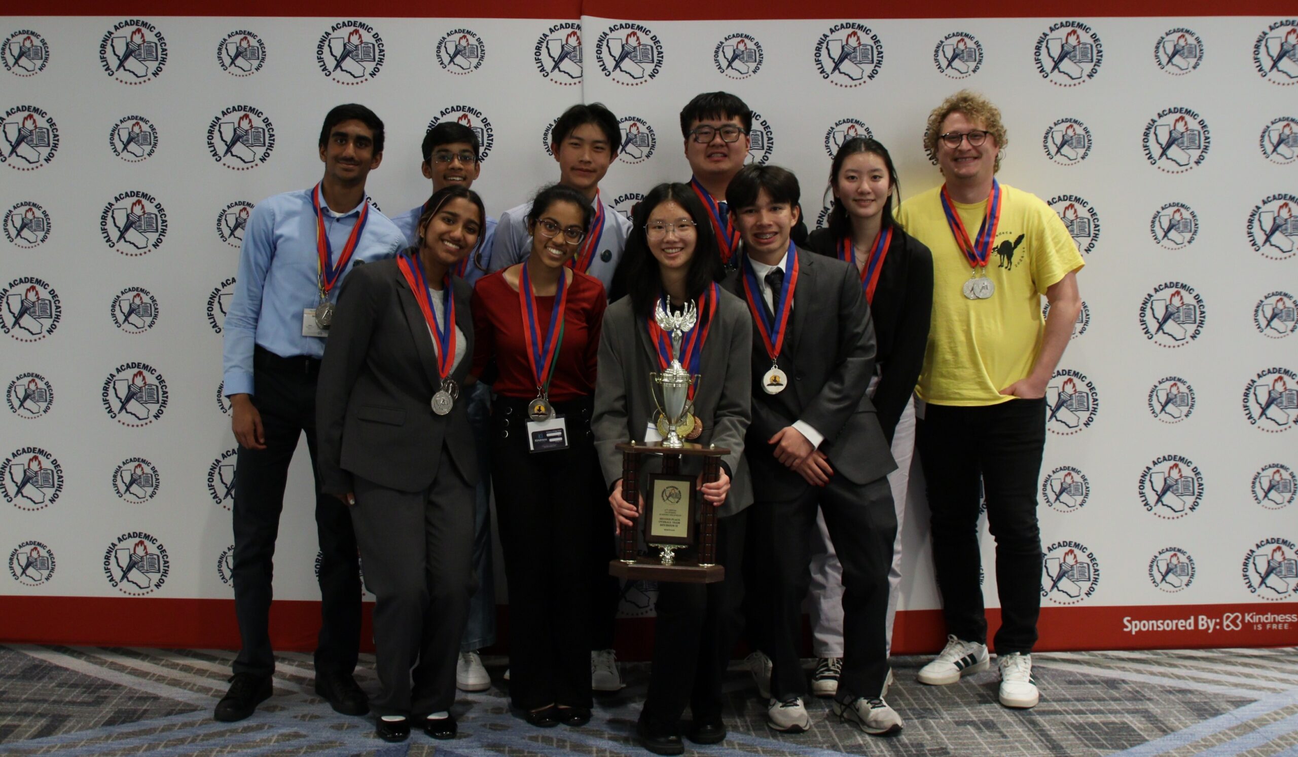Valencia High School students wearing medals pose with a trophy in front of a California Academic Decathlon backdrop.