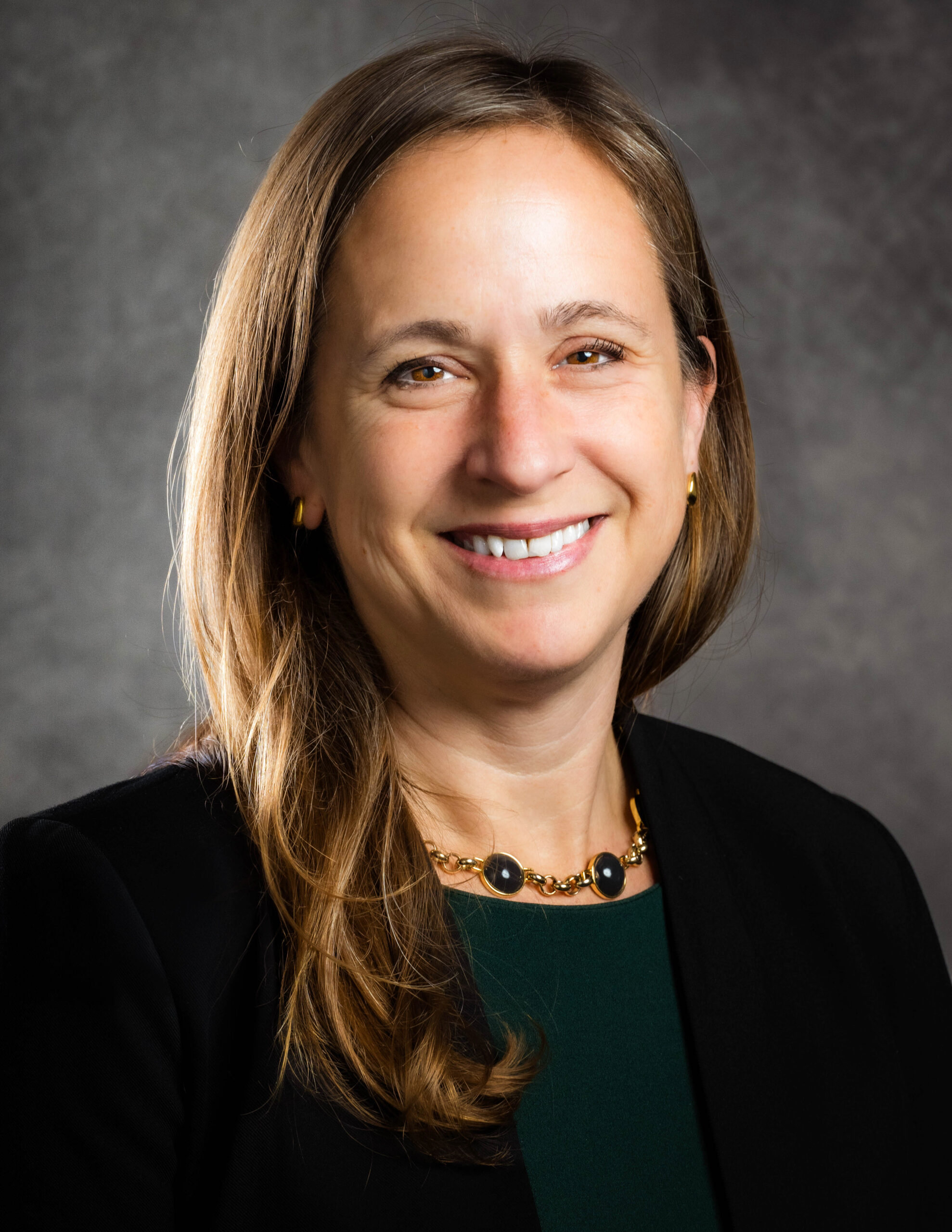 Portrait of Dr. Gretchen Janson wearing a dark blazer and green top against a neutral background.