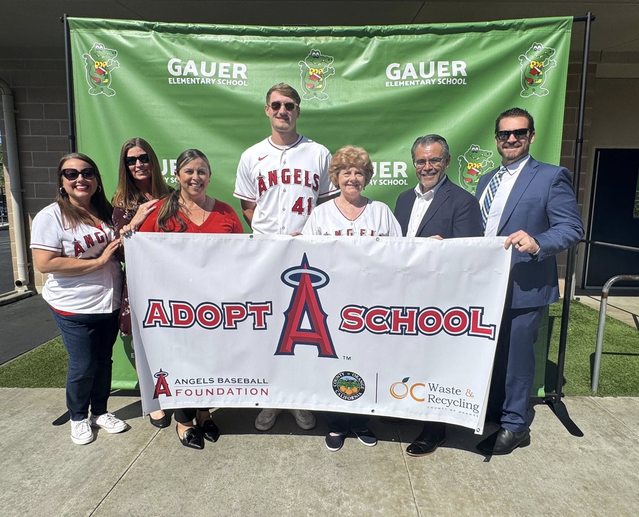 Trustee Alva Alvarez, Assistant Superintendent Dena Melland, Assistant Superintendent Dr. Yadira Moreno, Los Angeles Angels pitcher Jack Kochanowicz, Board President Jackie Filbeck, Superintendent Jesús Chavarria and Assistant Superintendent Matthew Slusser pose with an Angels Adopt-A-School banner at Gauer Elementary School in Anaheim.