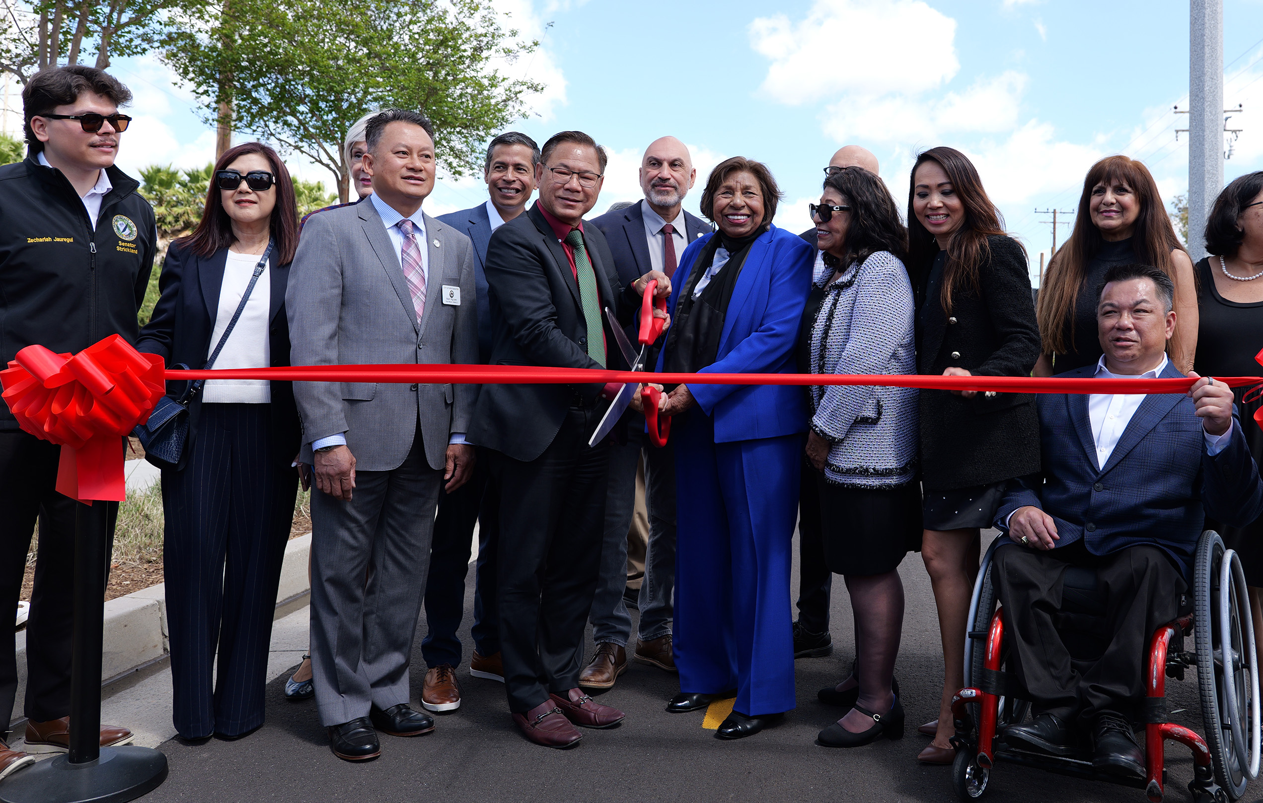 Sylvia Mendez and Westminster Mayor Chi Charlie Nguyen hold ceremonial scissors during a ribbon cutting for the Mendez Freedom Trail, joined by community leaders and partners.