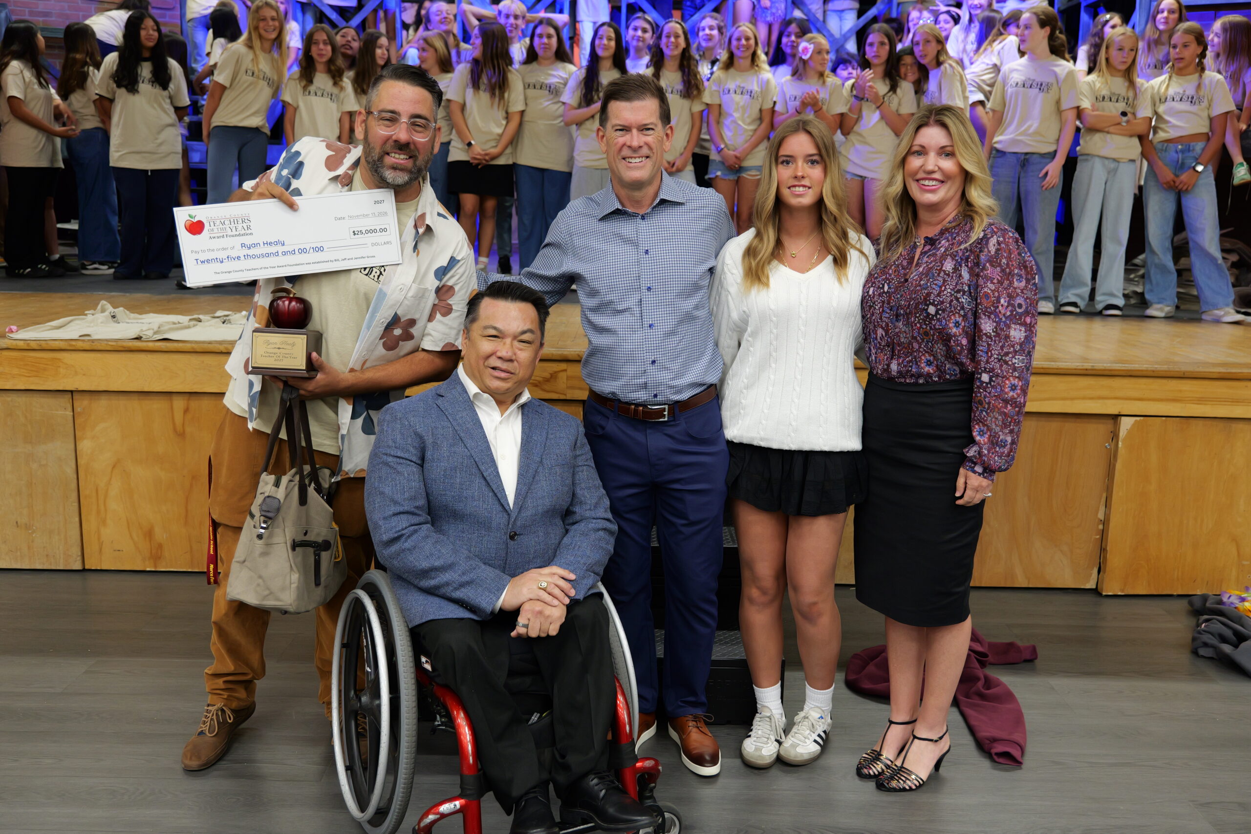 2027 Orange County Teacher of the Year Ryan Healy receives a $25,000 check from the William, Jeff and Jennifer Gross Family Foundation while receiving congratulations from Superintendent Dr. Bean and his Marco Forster Middle School musical theater students.