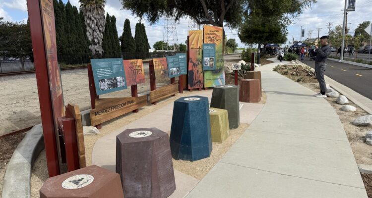 Interpretive panels and seating along the Mendez Freedom Trail in Westminster, as a man takes a photo and attendees gather in the background during the dedication ceremony.