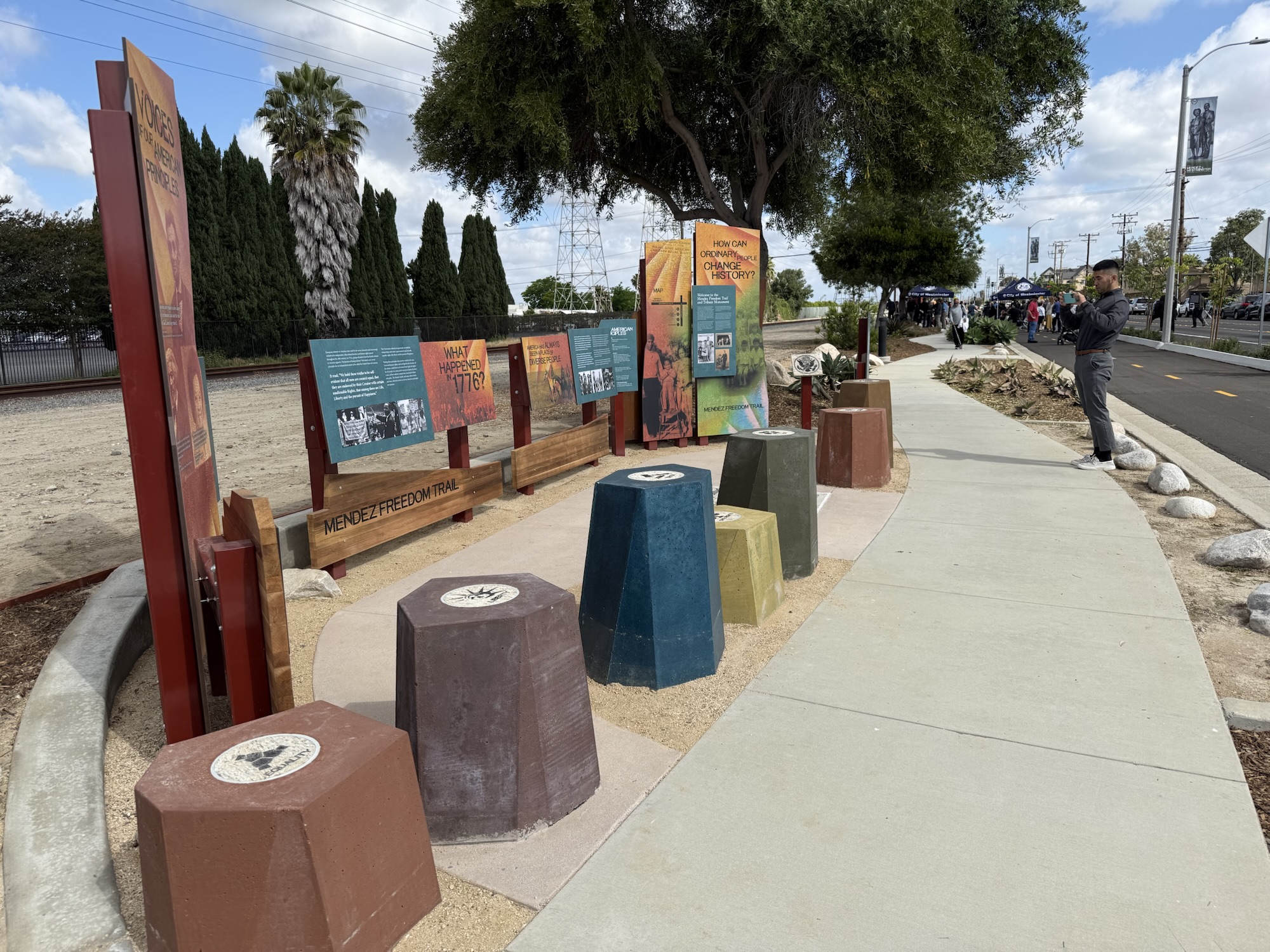 Interpretive panels and seating along the Mendez Freedom Trail in Westminster, as a man takes a photo and attendees gather in the background during the dedication ceremony.