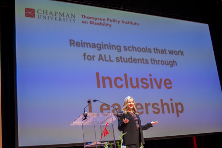 Kari Adams speaks onstage at the 2025 Thompson Policy Institute Summit on Disability and Inclusion at Chapman University, standing in front of a presentation screen displaying the words “Inclusive Leadership.”