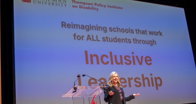 Kari Adams speaks onstage at the 2025 Thompson Policy Institute Summit on Disability and Inclusion at Chapman University, standing in front of a presentation screen displaying the words “Inclusive Leadership.”