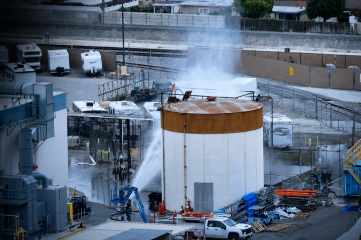 An aerial view shows emergency crews cooling a large industrial storage tank with water at the site of the Garden Grove chemical leak as mist rises from the facility.