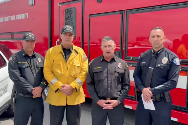 Four Orange County fire and law enforcement officials stand in front of an Orange County Fire Authority emergency response vehicle during a video briefing about the Garden Grove chemical leak response.