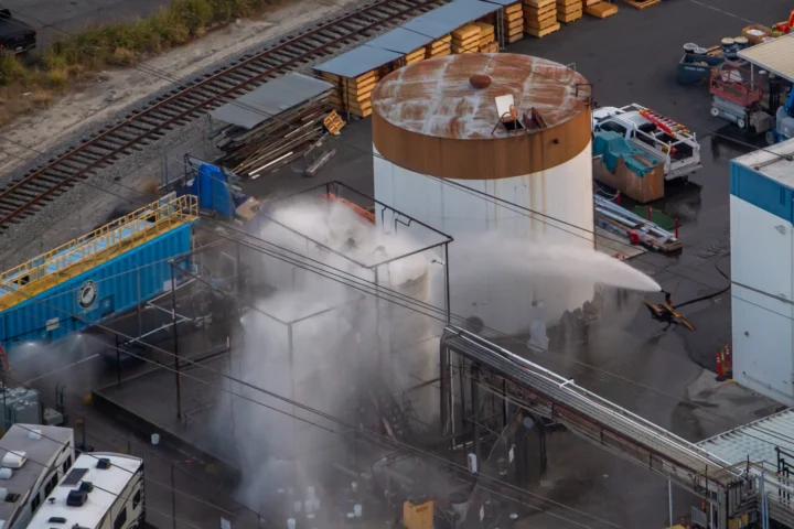 An aerial view shows emergency crews cooling a large industrial storage tank with water at the site of the Garden Grove chemical leak as mist rises from the facility.