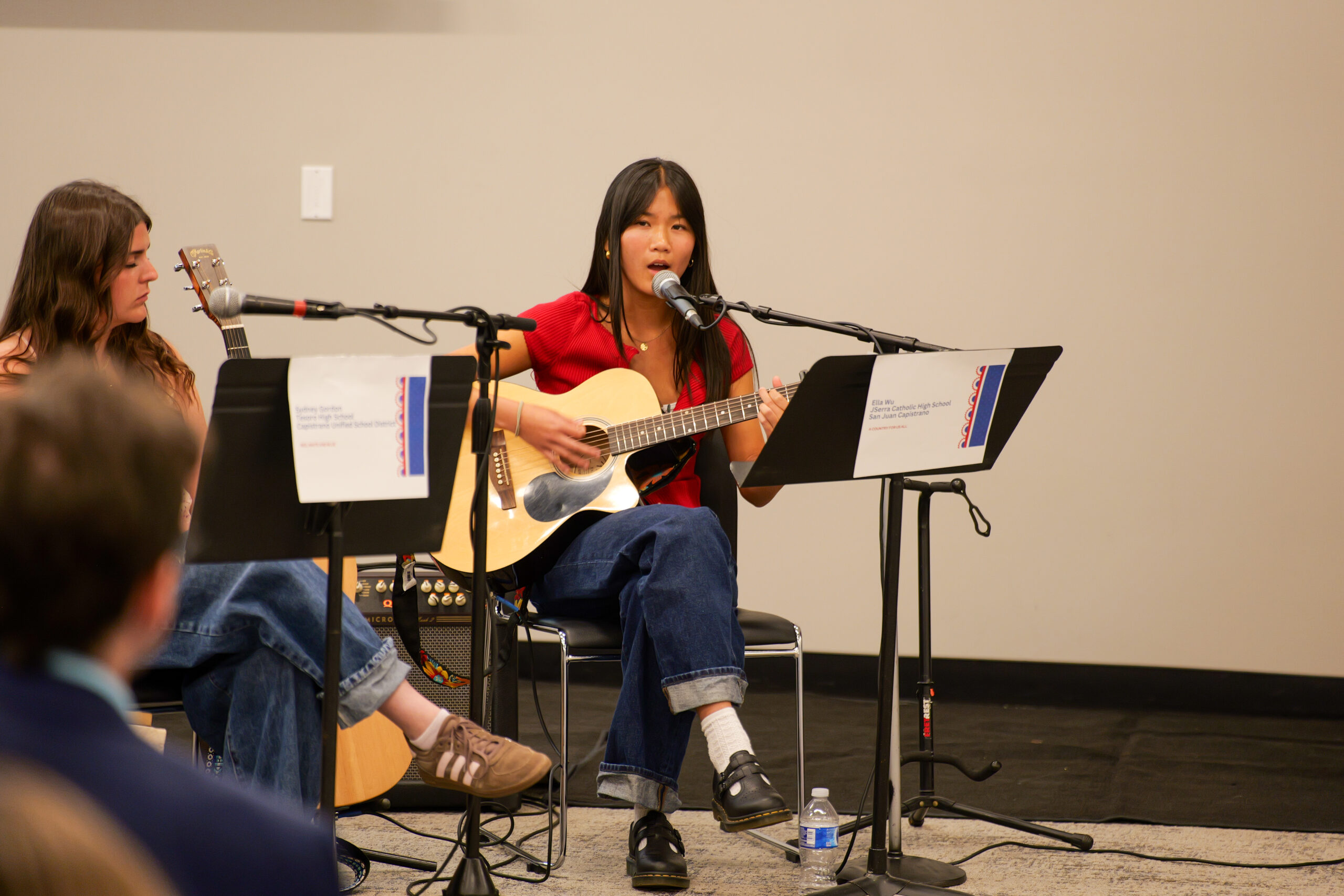 Ella Wu performs her original song, "A Country for Us All," on acoustic guitar during the USA 250-OC Theme Song Competition showcase.