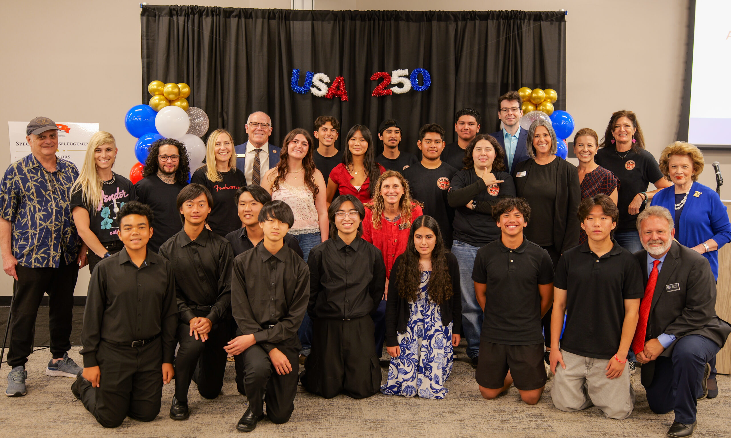 A group of students, educators, music professionals and community partners pose for a photo in front of a USA 250 backdrop during the USA 250-OC Theme Song Competition showcase and awards ceremony.