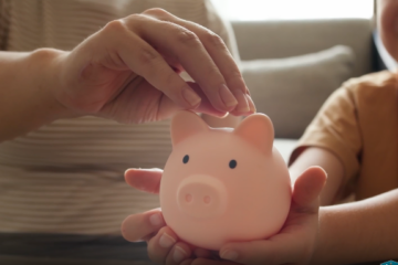 An adult and child place coins into a pink piggy bank, representing college and career savings opportunities available through the CalKIDS program.