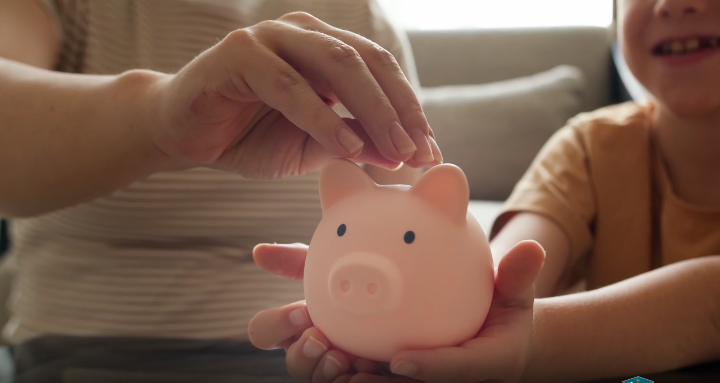 An adult and child place coins into a pink piggy bank, representing college and career savings opportunities available through the CalKIDS program.